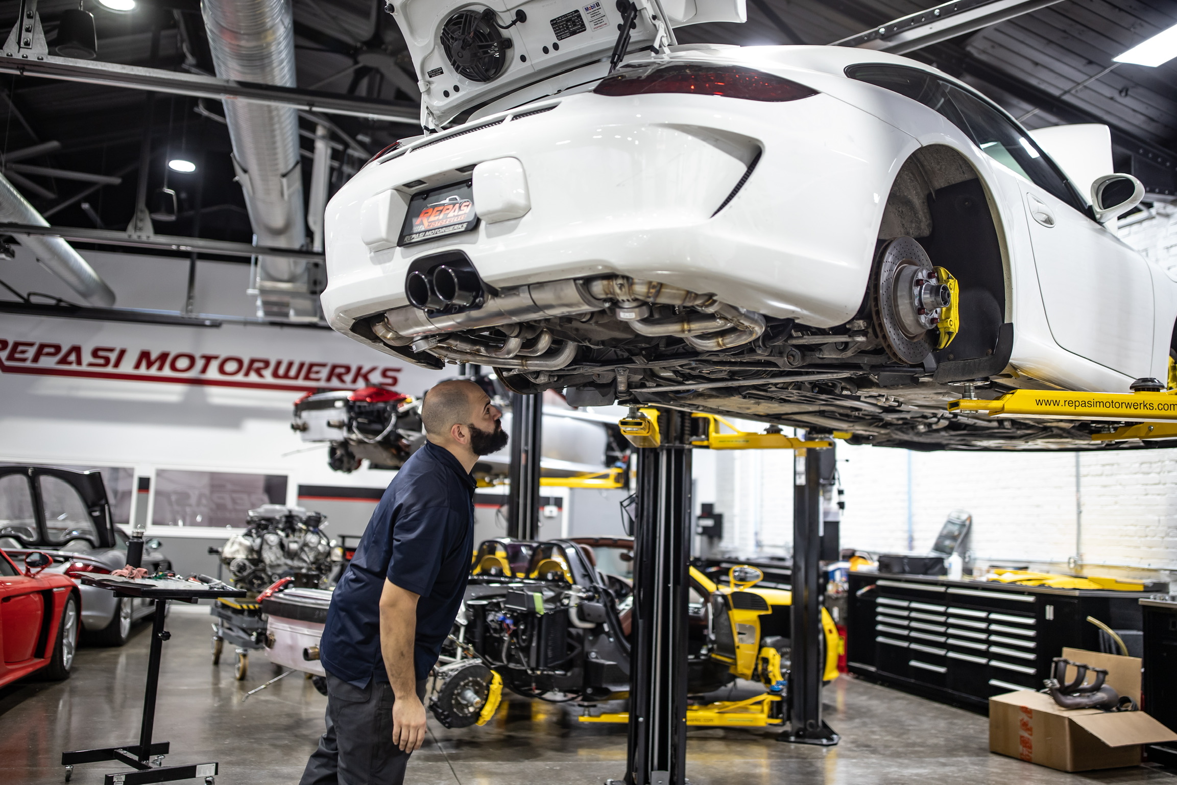 Technician inspecting the underside of a white Porsche 991 GT3 on the lift during a pre-purchase inspection